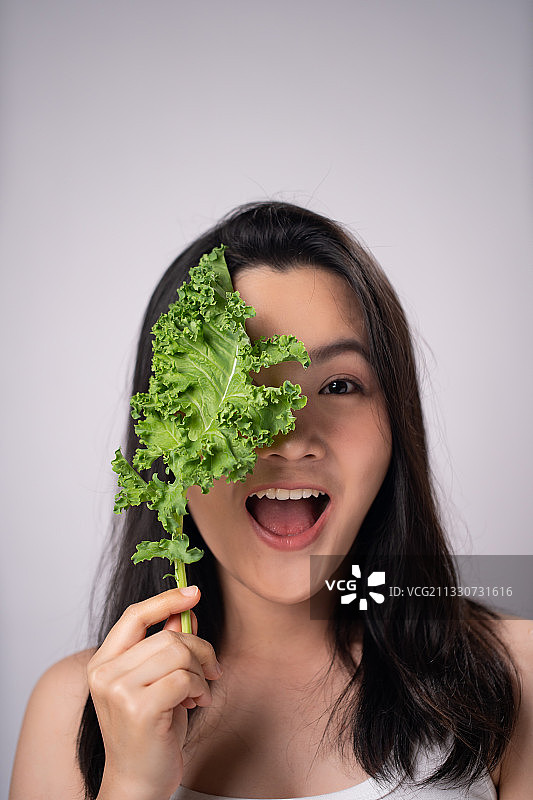 在白色背景下吃蔬菜的微笑年轻女性的肖像图片素材