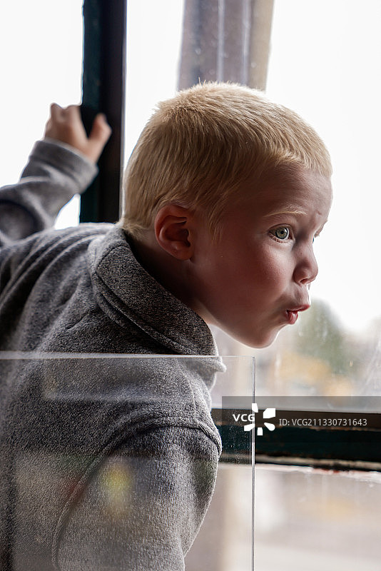 男孩在家中透过窗户向外看的侧视图，美国俄勒冈州尤金图片素材