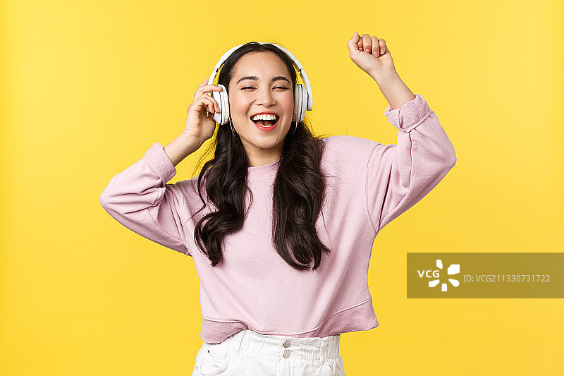 在黄色背景下听音乐的微笑年轻女子图片素材