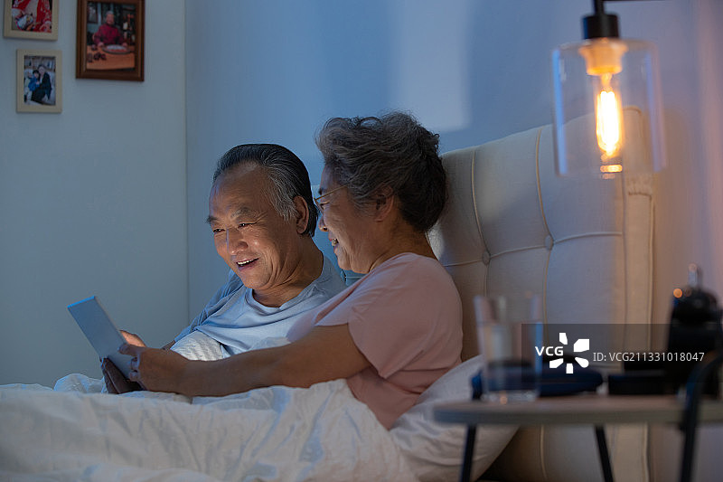 老年夫妇坐在床上用平板电脑看视频图片素材