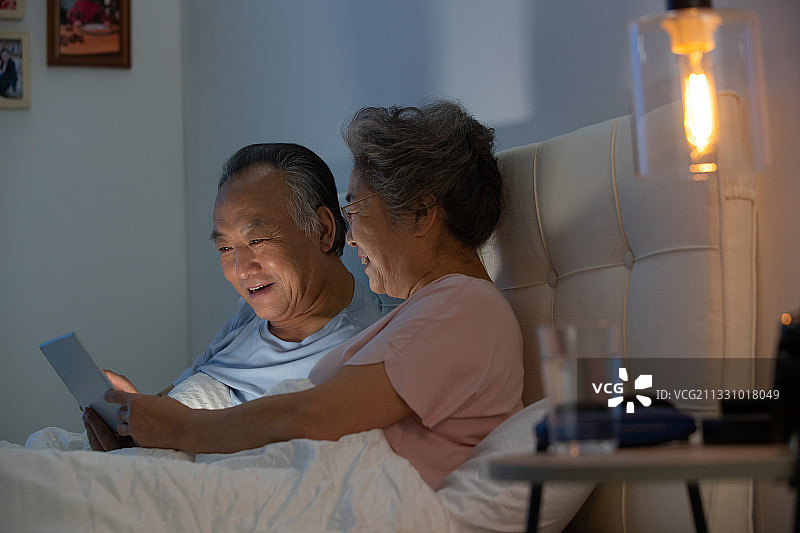 老年夫妇坐在床上用平板电脑看视频图片素材