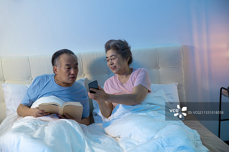 老年夫妇坐在床上看手机图片素材