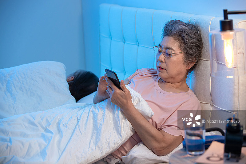 老年人坐在床上看手机图片素材