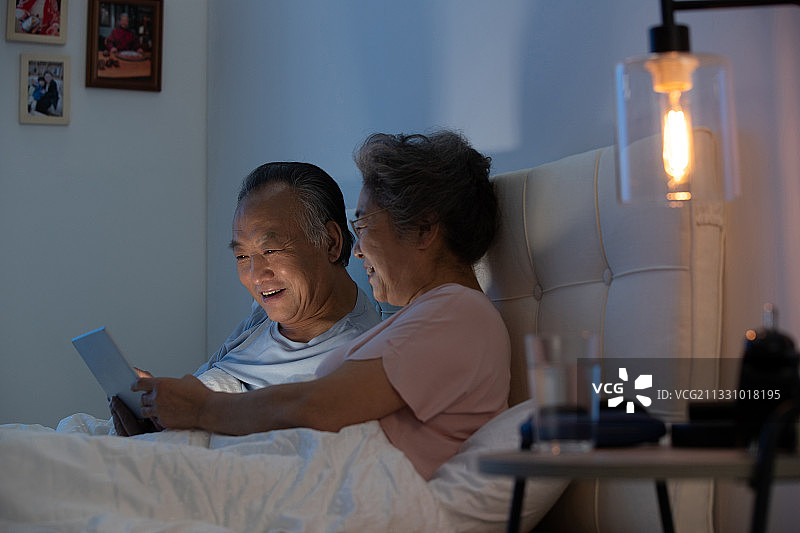 老年夫妇坐在床上用平板电脑看视频图片素材