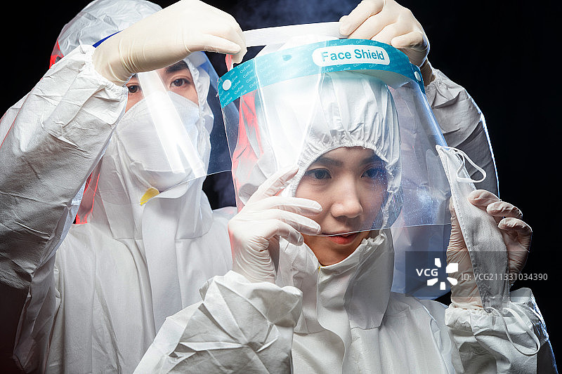 穿防护服的青年男人帮同事戴面罩图片素材