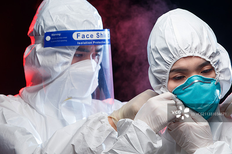穿防护服的青年男人帮同事调节口罩图片素材