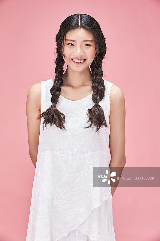 粉色背景前的身穿白色连衣裙的活力亚洲少女图片素材