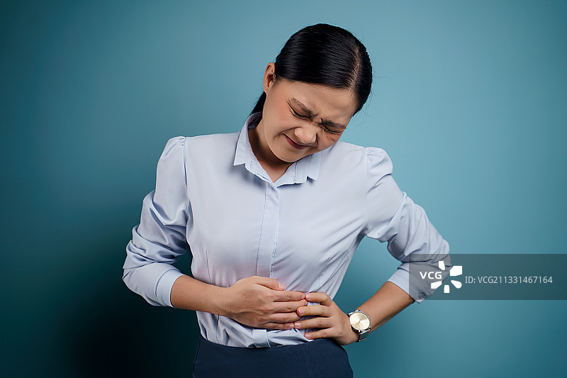 胸口疼痛，靠在蓝色背景前的年轻女人图片素材