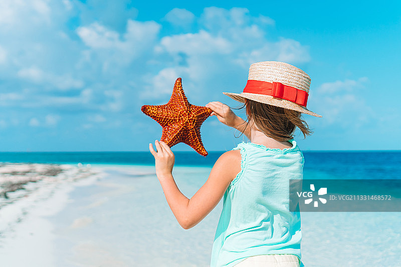 女孩在海滩拿着海星仰望天空图片素材