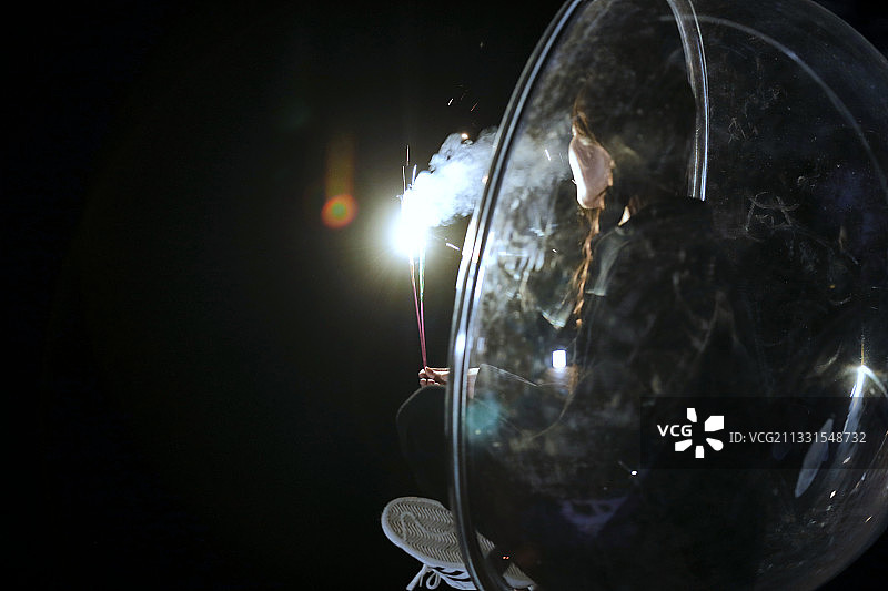 夜晚坐在透明秋千上燃放仙女棒的可爱少女图片素材