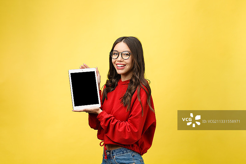 微笑的女人在黄色背景下手持平板电脑的肖像照图片素材
