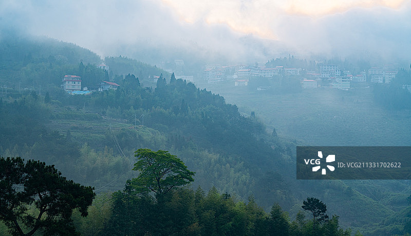 绿树前大山上朝阳和晨雾笼罩着的乡村，朦胧如刚苏醒的婴儿。图片素材
