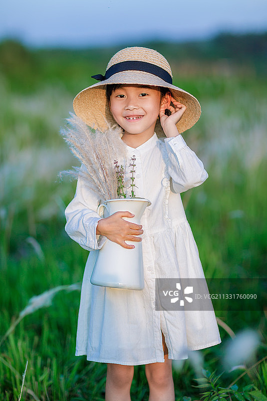 穿白色连衣裙戴草帽的小女孩在户外草丛中玩耍图片素材