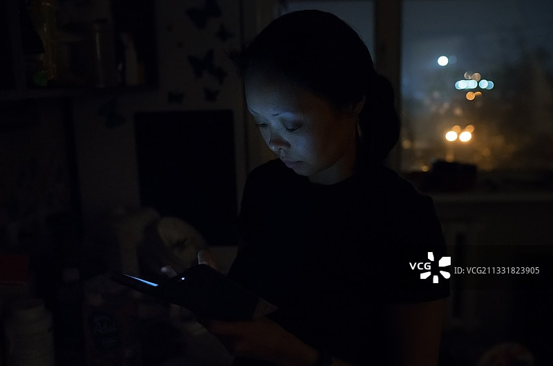 女人在黑暗的房间里晚上使用智能手机图片素材