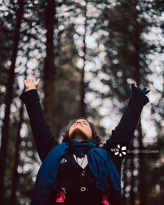 秘鲁卡哈马卡：女子张开双臂站在森林树木前的仰视角度照片图片素材