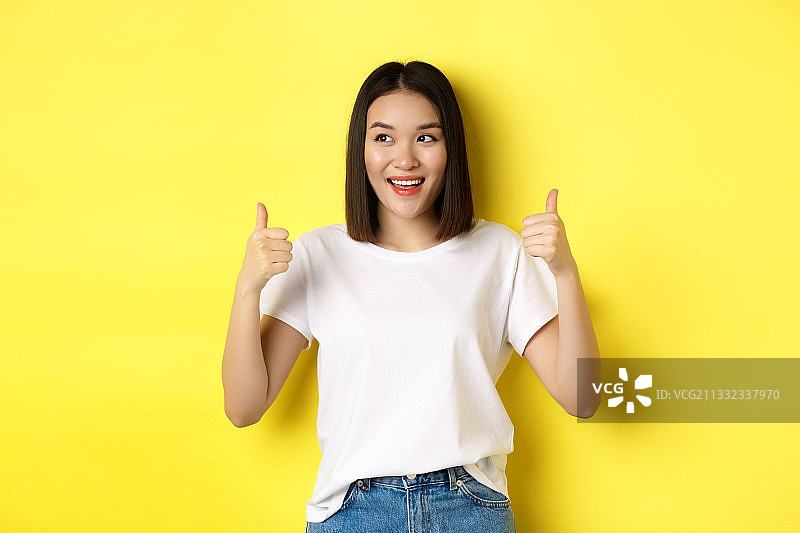 站在黄色背景下手势的微笑年轻女性肖像图片素材