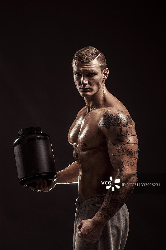 赤膊健壮男人手拿蛋白奶昔对着黑色背景图片素材