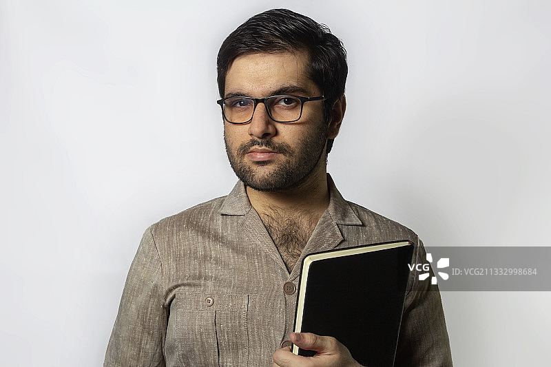站在白色背景下拿着书的年轻男人肖像，巴基斯坦旁遮普邦拉合尔图片素材