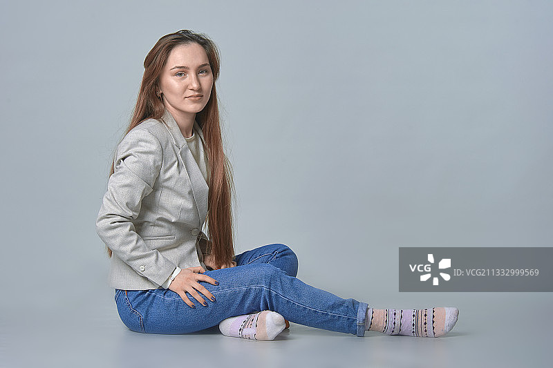 年轻女人在灰色背景的影棚中就坐图片素材
