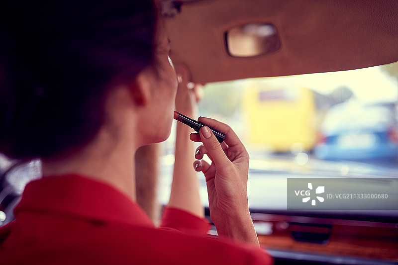 坐在车里涂口红的穿红色西装的年轻女商人图片素材
