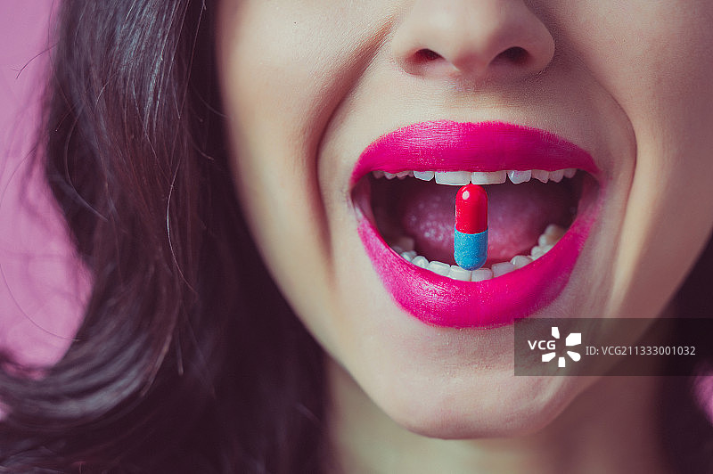 特写：涂着粉色口红，手拿药丸的女人图片素材