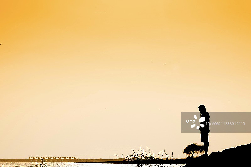 日落时，站在印度马哈拉施特拉邦纳西克邦的田野上，以晴朗的天空为背景的男子剪影图片素材