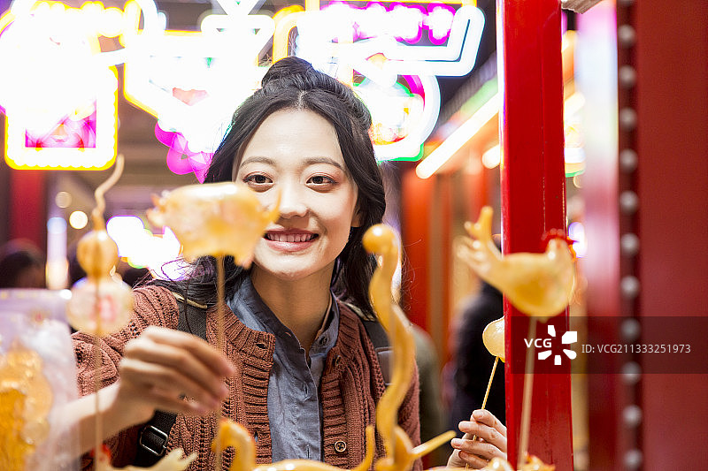 青年女子城市美食街旅行买糖人图片素材