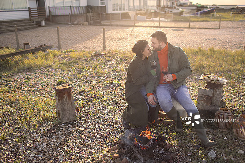 穿着冬季外套的情侣在海滩露台上享受篝火旁的葡萄酒图片素材