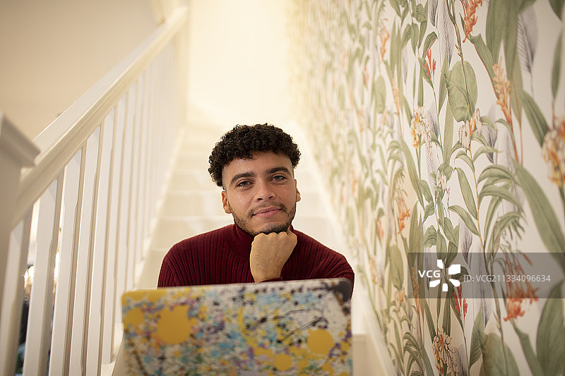 在家中楼梯上使用笔记本电脑的自信年轻人肖像图片素材