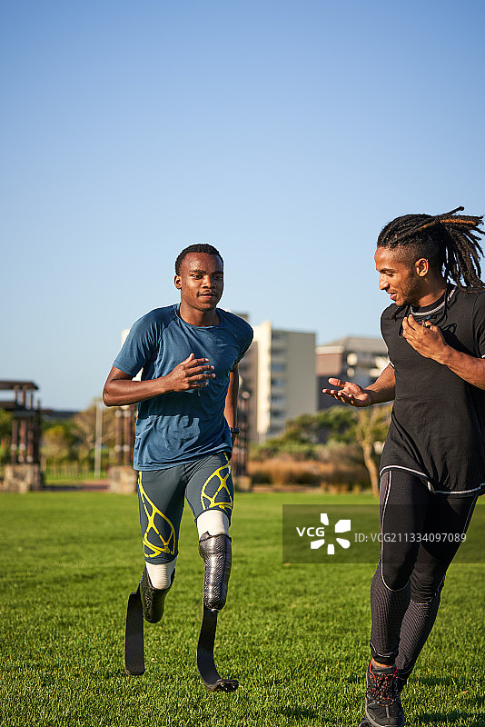 教练为在阳光草地上跑步的截肢运动员计时图片素材