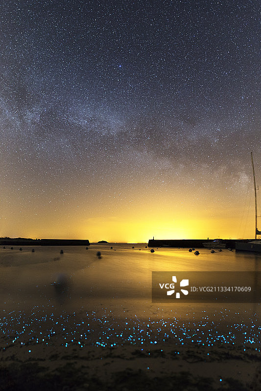 岸边发光的磷光浮游生物，小浪花拍打着海岸。天空中的银河，盛夏时节。图片素材