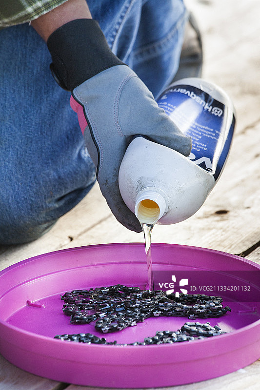 冬季设备维护：将链锯链条浸泡在链条油中，防止生锈腐蚀并保证其柔韧性图片素材