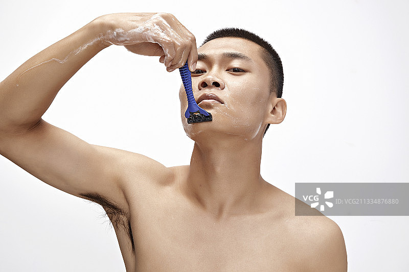 白色背景下手持剃须刀在刮胡子的亚洲男性图片素材