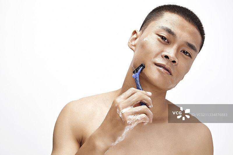 白色背景下手持剃须刀在刮胡子的亚洲男性图片素材