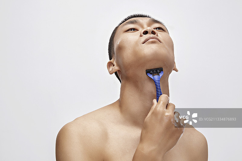 白色背景下手持剃须刀在刮胡子的亚洲男性图片素材