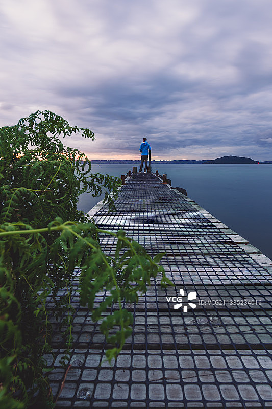 男人站在海上的码头上，背景是天空，新西兰罗托鲁瓦图片素材
