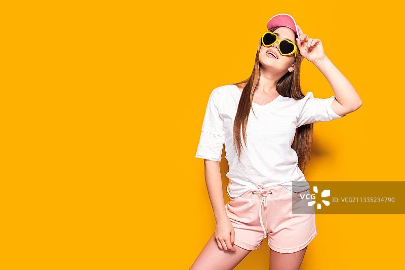 站在黄色背景前戴太阳镜的年轻女子微笑图片素材