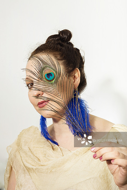 手持孔雀羽毛遮面的女子肖像图片素材