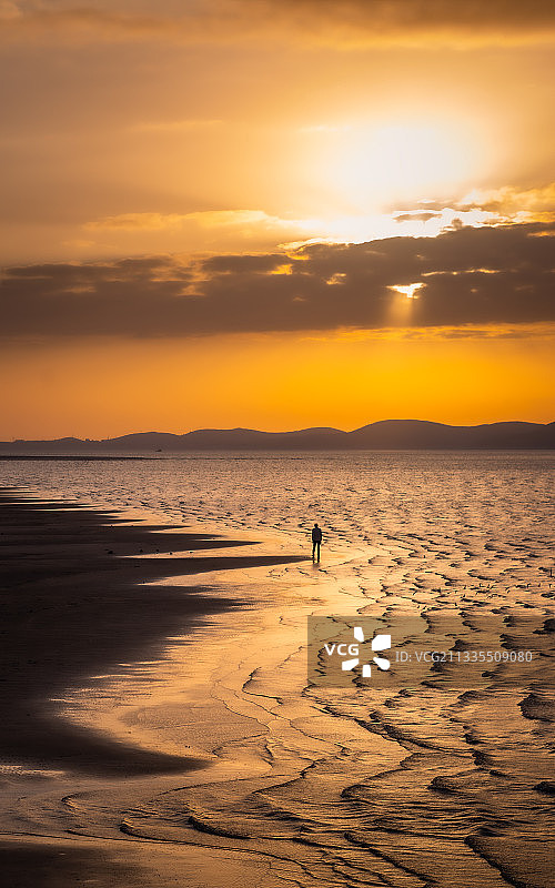 黄昏夕阳西下时，一个人独自在海边沙滩上徘徊的孤独背影图片素材