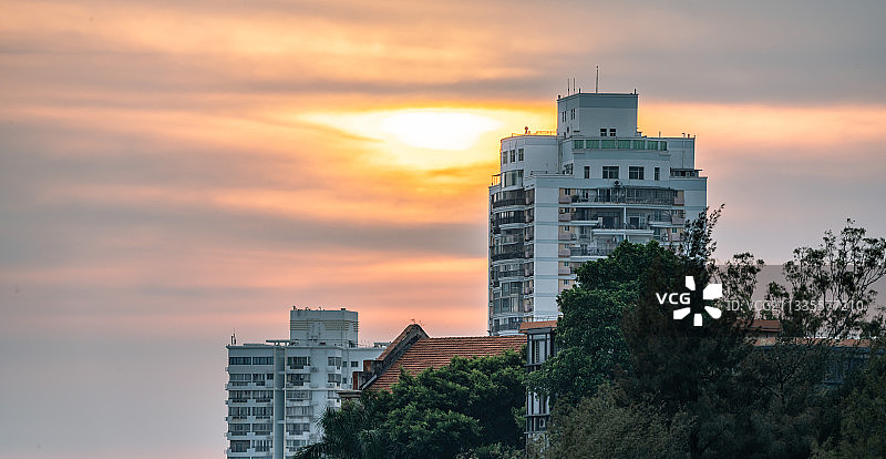 夕阳里的建筑，在红色天空和绿树的映衬下，白色方形建筑沉静坚毅图片素材