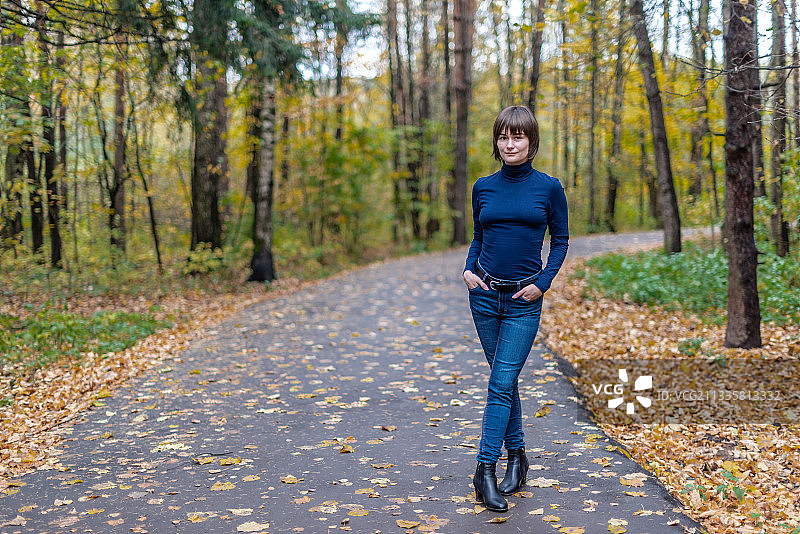 秋季森林中站在人行道上微笑的女人肖像图片素材