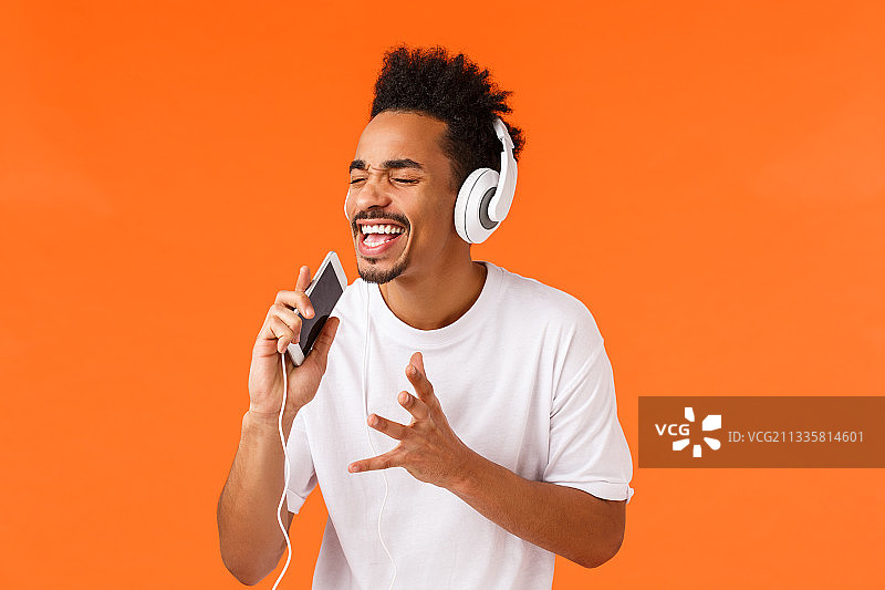 在橙色背景下听音乐的微笑青年图片素材