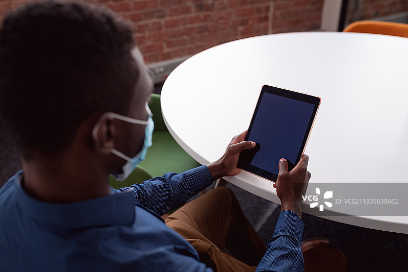 戴着口罩的非裔美国男商人坐在会议室的桌旁使用平板电脑图片素材