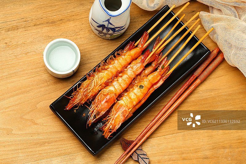 黑色盘子里的烤虾和清酒酒壶图片素材