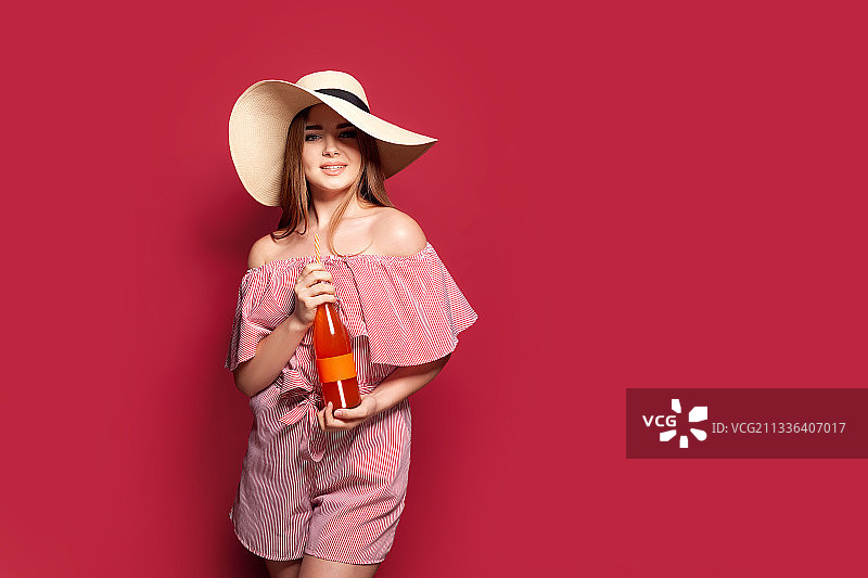 穿着红色连衣裙，拿着一瓶橙色饮料的漂亮年轻女子图片素材