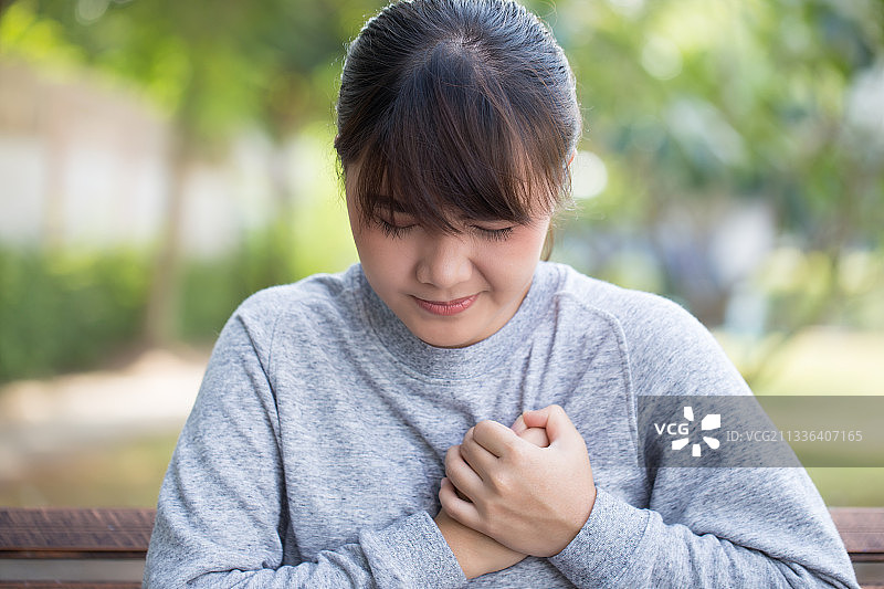 年轻女人坐在公园长椅上感到疼痛图片素材