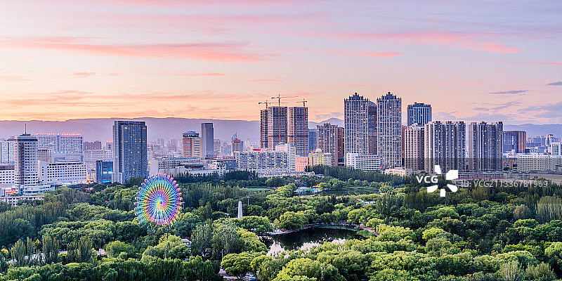 中国内蒙古呼和浩特青城公园旋转的摩天轮和城市天际线晚霞图片素材