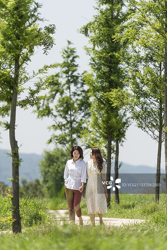 母女牵手走在树木林荫道上图片素材