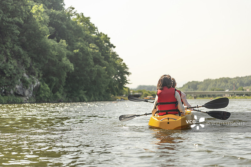 两名戴着太阳镜和救生衣的女子在河上划皮划艇图片素材