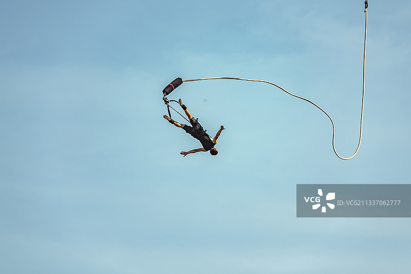 低角度观看男子在空中伸出双臂进行蹦极图片素材